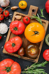 Board with different fresh tomatoes on black background