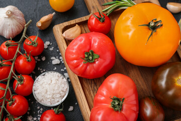 Board with different fresh tomatoes on black background