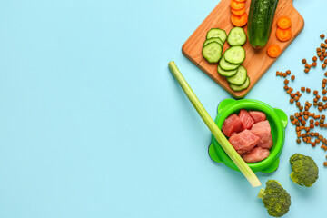 Composition with dry pet food, raw meat and natural products on blue background
