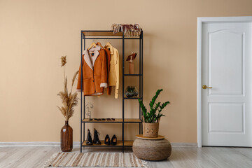 Shelving unit with clothes and shoes near beige wall in hall
