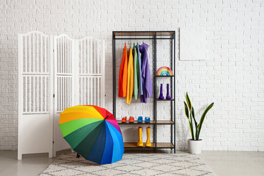 Interior of stylish room with shelving unit, clothes and umbrella - Powered by Adobe