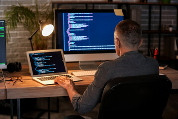Mature male programmer working in office at night, back view