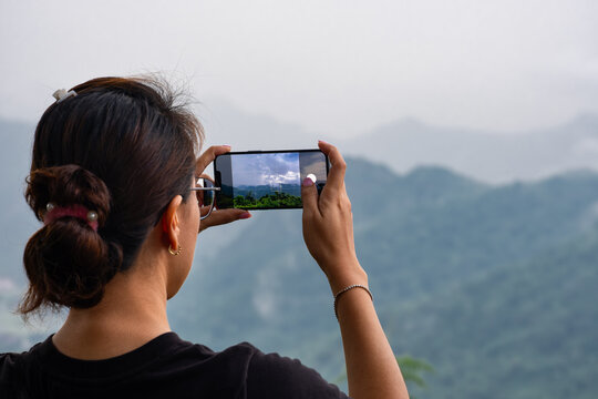 A woman uses her smartphone to take pictures of the sunrise in a valley with abundant nature tourism and technology