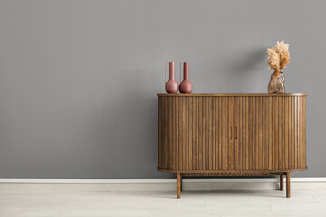 Wooden chest of drawers with pampas grass and decor near grey wall in room
