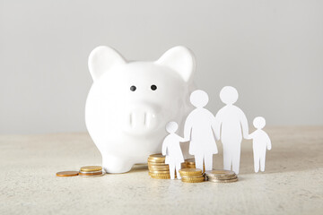 Figures of family with piggy bank and coins on light table. Savings concept