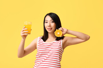 Beautiful Asian woman with orange and glass of juice on yellow background