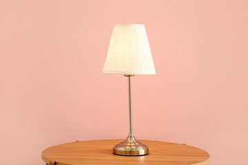 Glowing lamp on wooden table near pink wall