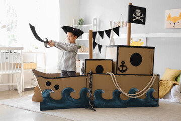 Cute little pirate playing with sword in cardboard ship at home