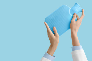 Female doctor's hands with hot water bottle on blue background
