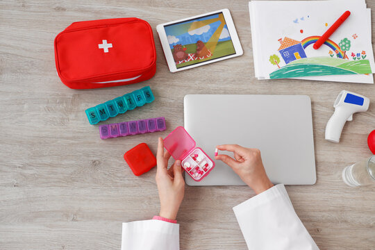 Female doctor hands with laptop, pills, first aid kit and pictures at grey table