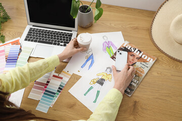 Fashion designer working at table with mobile phone, cup of coffee, color swatches and laptop