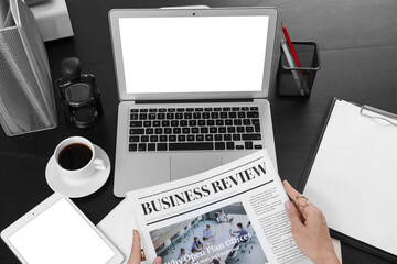 Businesswoman reading newspaper at workspace with laptop and cup of coffee