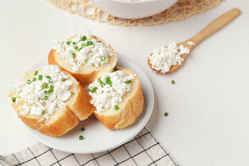 Baguette pieces with cottage cheese and green onion on plate, closeup