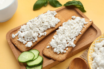 Tasty crispbread with cottage cheese and cucumber on yellow table