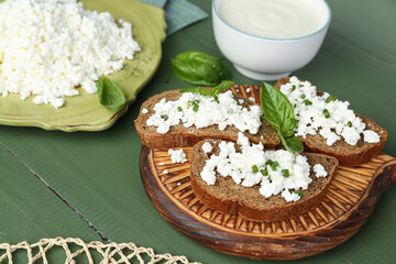 Fototapeta na wymiar Tasty sandwiches with cottage cheese and basil leaves on green wooden table