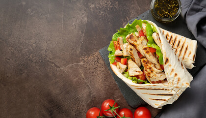 Shawarma pita bread with grilled chicken, fresh vegetables and cream sauce on a background of brown...