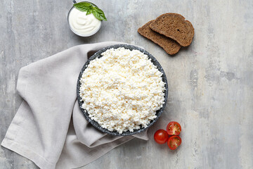 Fresh cottage cheese in bowl with sour cream, bread pieces and tomatoes on grey table