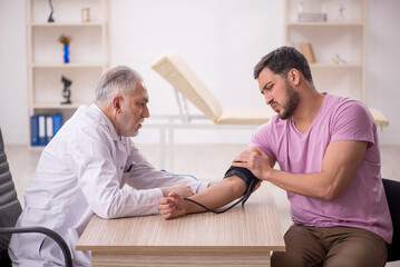 Obraz premium Old male doctor measuring young patient's blood pressure