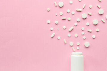 Different pills spilling out of pill bottle on pink background