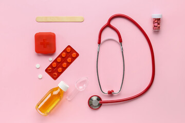 Red stethoscope, bottle and pills on pink background