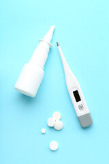 Pills, nasal spray and thermometer on blue background