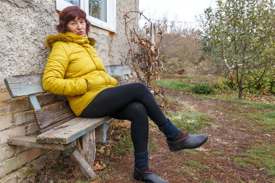 portrait of a beautiful mature woman sitting on a bench near her house on an autumn day