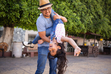hispanic dad and daughter smiling having fun at the park on summer, father carrying and playing...