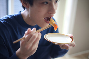 海老天のしっぽを食べる男性