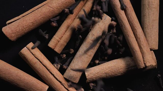 Fragrant spices, cinnamon sticks, dried cloves fall on a black background close-up of slowmo.