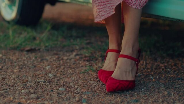Close-up of women's legs in red shoes getting out of a retro car