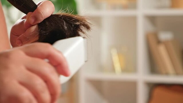 Hair cutting at home. Barber shop at home. A woman cuts her own hair with a clipper. Cutting dry split ends of hair.