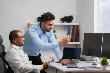 Indian stock brokers or traders discussing from stock market chart or doing technical analysis on monitor at office - concept of teamwork, Investment Decisions and Data Analysis