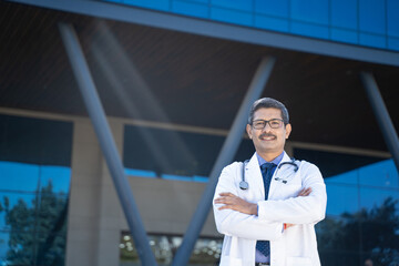 medical concept. Confident Indian doctor standing out of hospital.