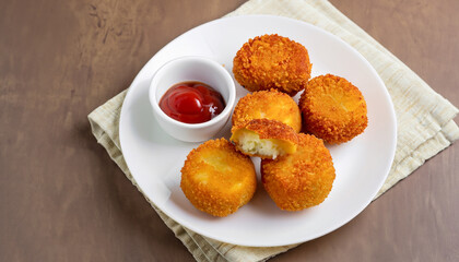 delicious potato croquettes - mashed potatoes balls with grated mozzarella cheese seasoned with spices; breaded and deep fried in olive oil, served with ketchup on white plate, view from above
