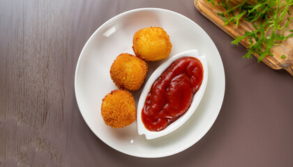 delicious potato croquettes - mashed potatoes balls with grated mozzarella cheese seasoned with spices; breaded and deep fried in olive oil, served with ketchup on white plate, view from above
