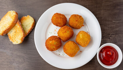 delicious potato croquettes - mashed potatoes balls with grated mozzarella cheese seasoned with spices; breaded and deep fried in olive oil, served with ketchup on white plate, view from above
