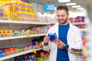 Young indian man looking product detail and purchasing at grocery shop.
