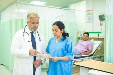 Senior doctor discussing with female assistant after checking patient at hospital