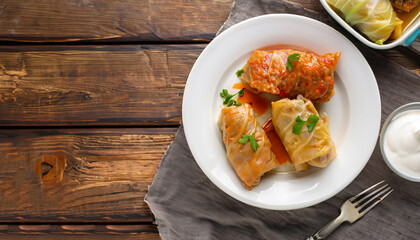 cabbage rolls stuffed with ground beef and rice served on a white plate on an old rustic table with sour cream in a bowl, view from above, close-up, flatlay