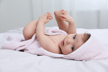 Cute little baby in hooded towel after bathing on bed at home