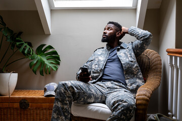 African american male soldier wearing military uniform sitting and using smartphone at home