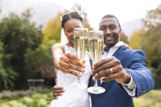 Happy african american bride and groom toasting with champagne at wedding in sunny garden