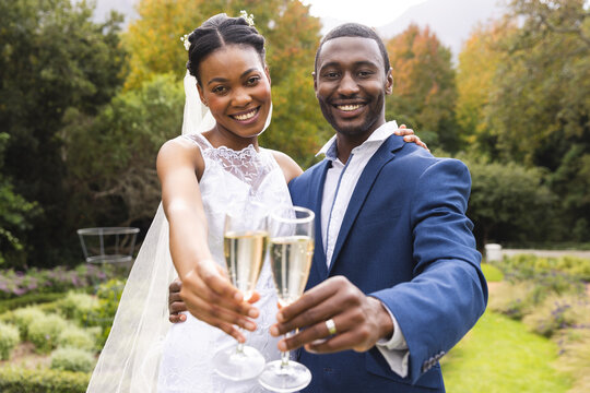 Portrait of happy african american bride and groom toasting with champagne in sunny garden