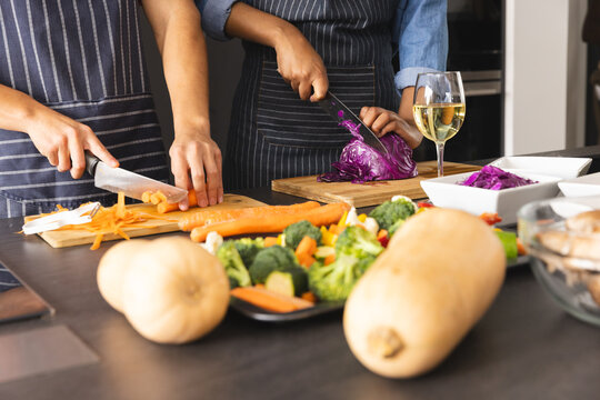 Midsection of diverse couple in aprons preparing meal, chopping vegetables in kitchen