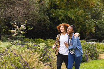 Happy diverse couple embracing and walking in garden, copy space