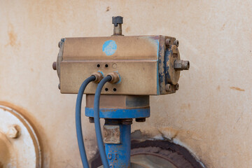 Photograph of an old and dirty motor controller on a water truck bolted to a blue steel flange and pipe with control cables connected to the control box