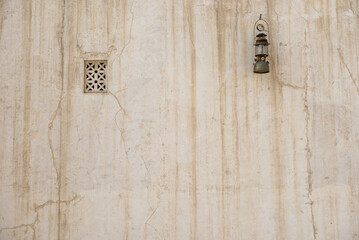 Front view of grunge, old wall of an Arabic heritage house. A vintage gas lamp hanging on the weathered wall with tiny window from a Middle Eastern architecture.