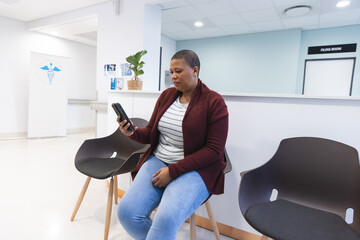 Worried african american female patient using smartphone in waiting room at hospital