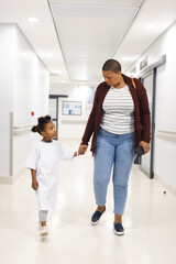 African american girl patient and her mother walking in corridor at hospital