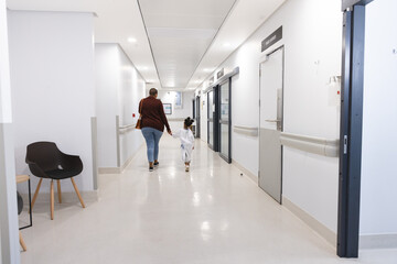 African american girl patient and her mother walking in corridor at hospital